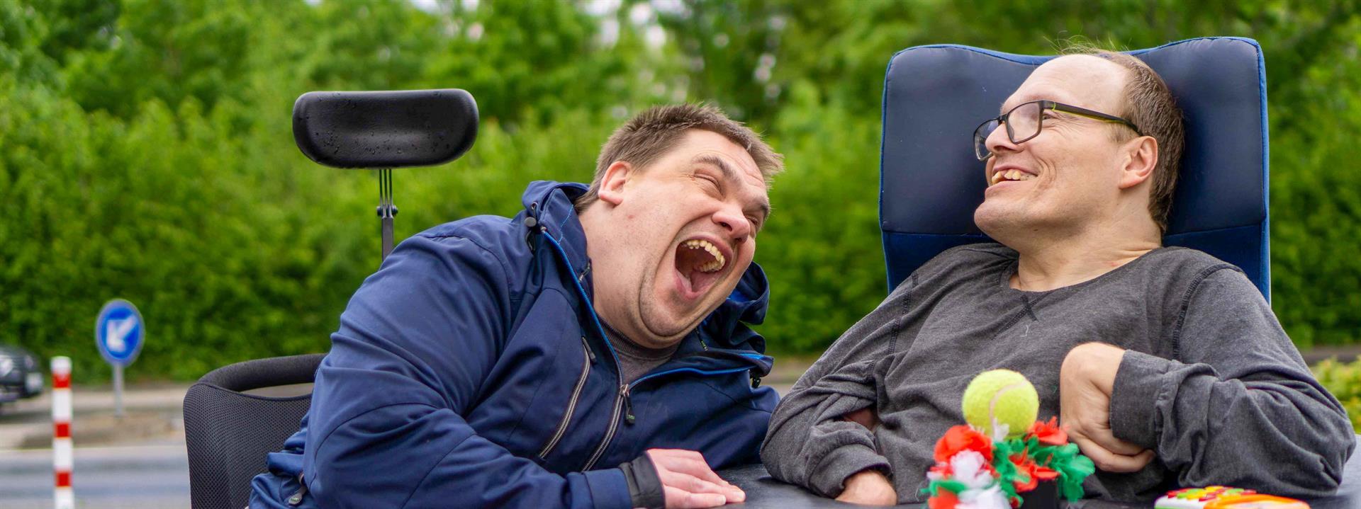 Foto von zwei Männern im Rollstuhl die herzlich lachen